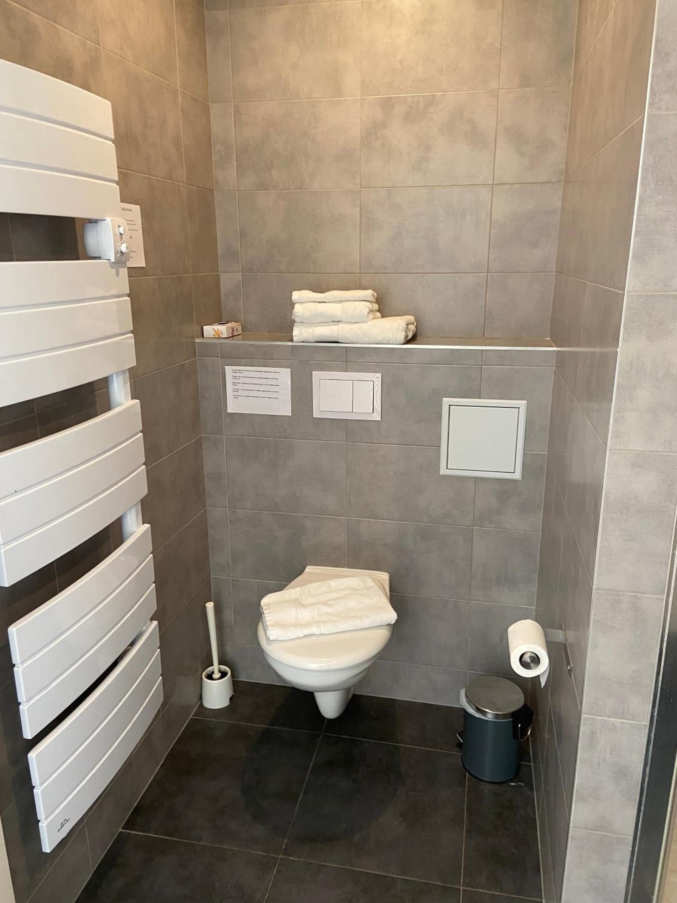 A modern bathroom with a toilet, a bidet, a towel rack, and a trash bin.