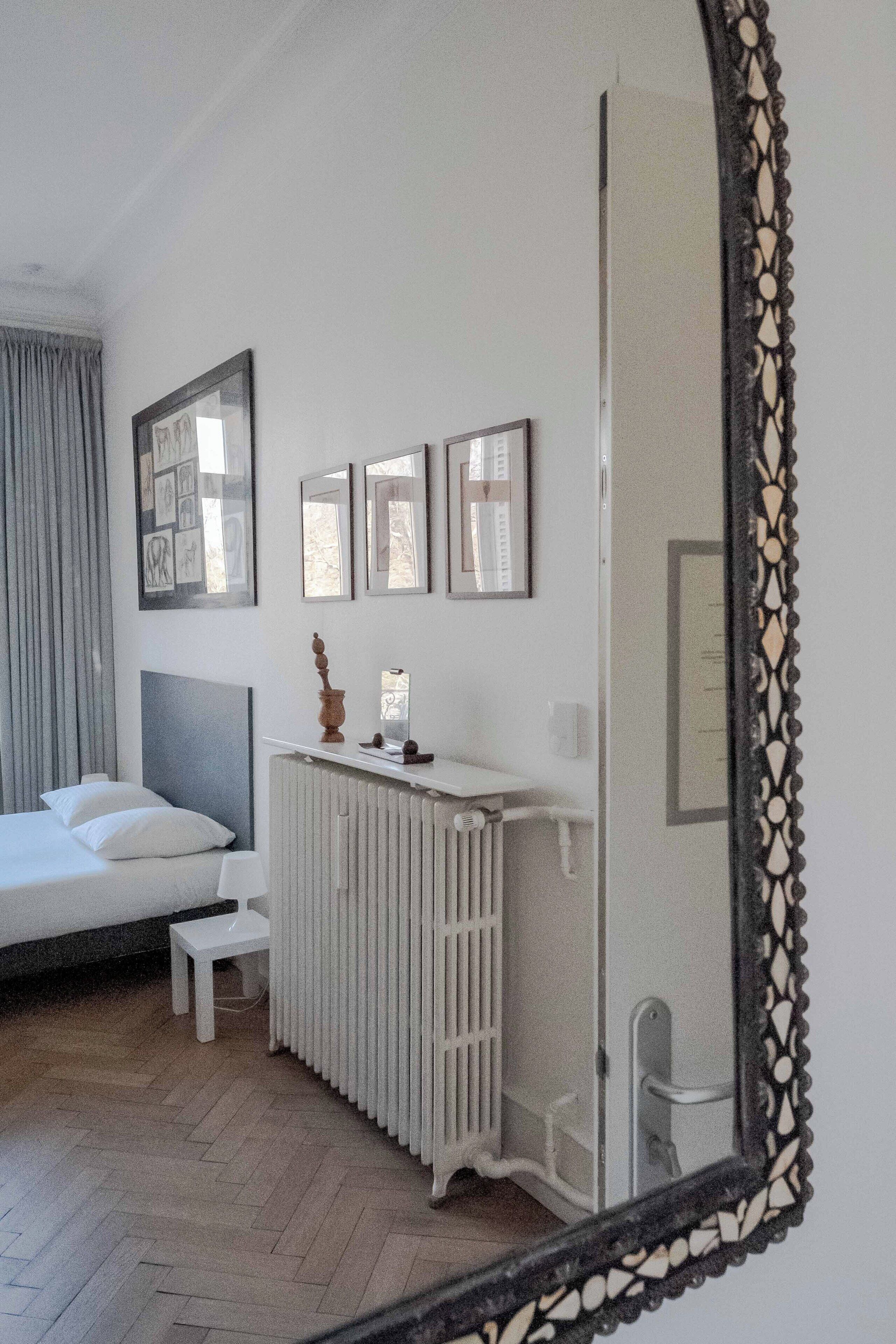 Une chambre à coucher comprenant un lit, un radiateur, une petite table et un miroir avec un cadre décoratif.