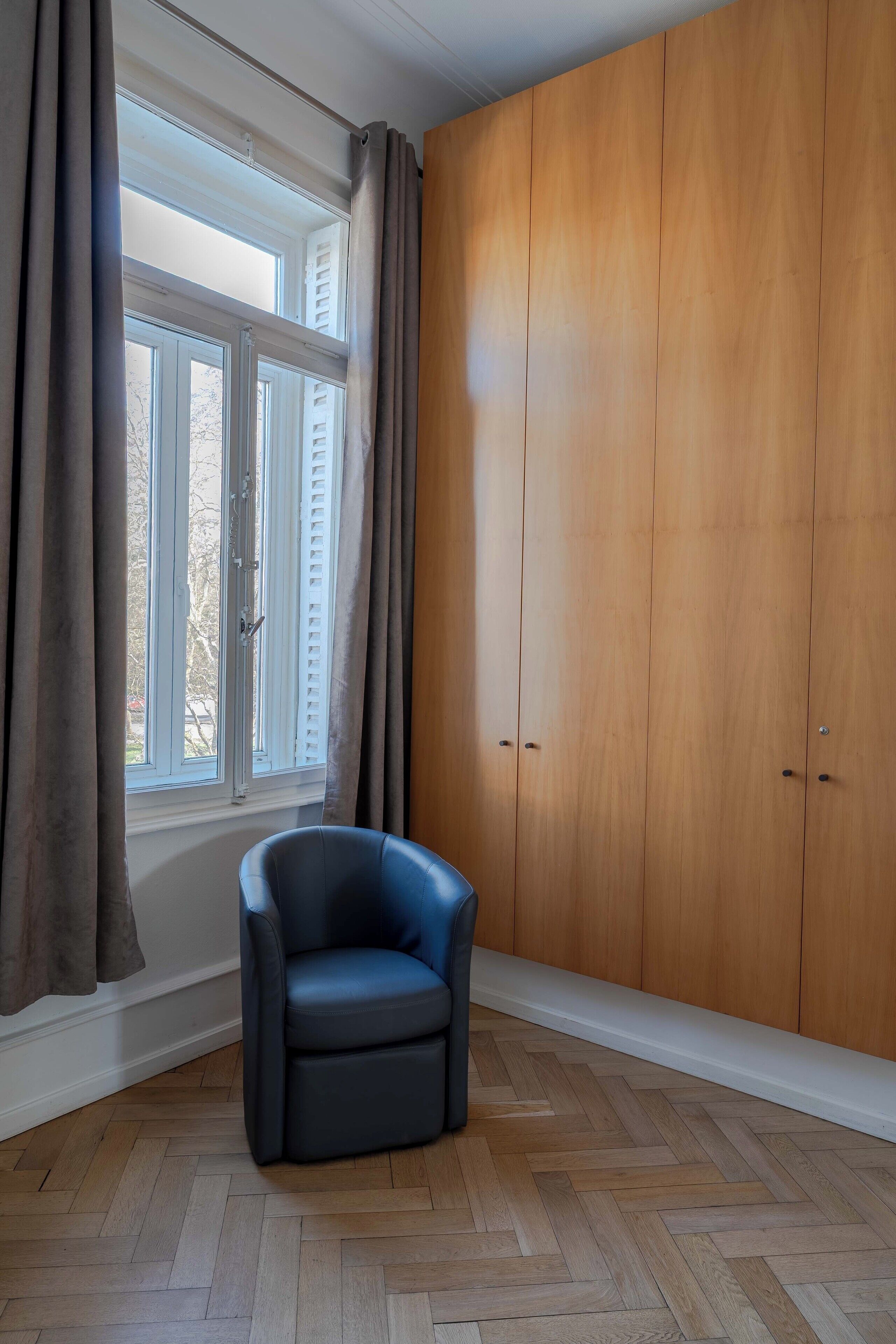 Une pièce avec une grande armoire, une chaise et une fenêtre avec des rideaux.
