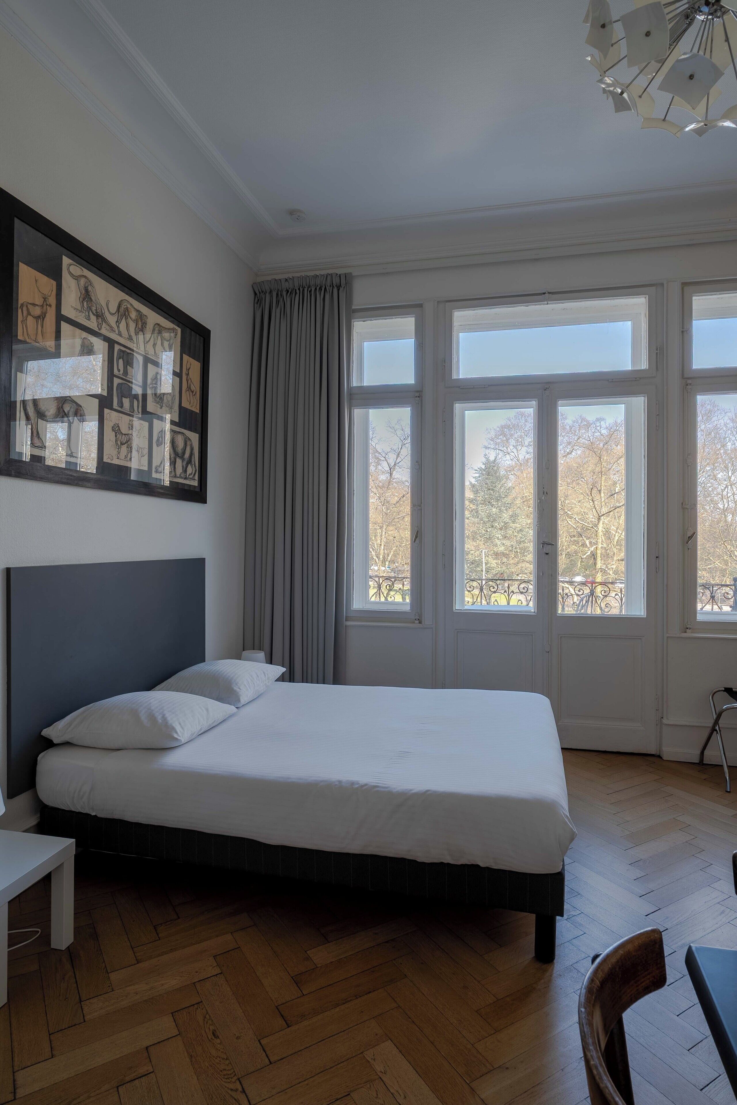 A bedroom with a large bed, a headboard, a bedside table, and a window with curtains.