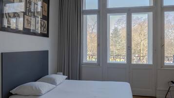 A bedroom with a large bed, a headboard, a bedside table, and a window with curtains.