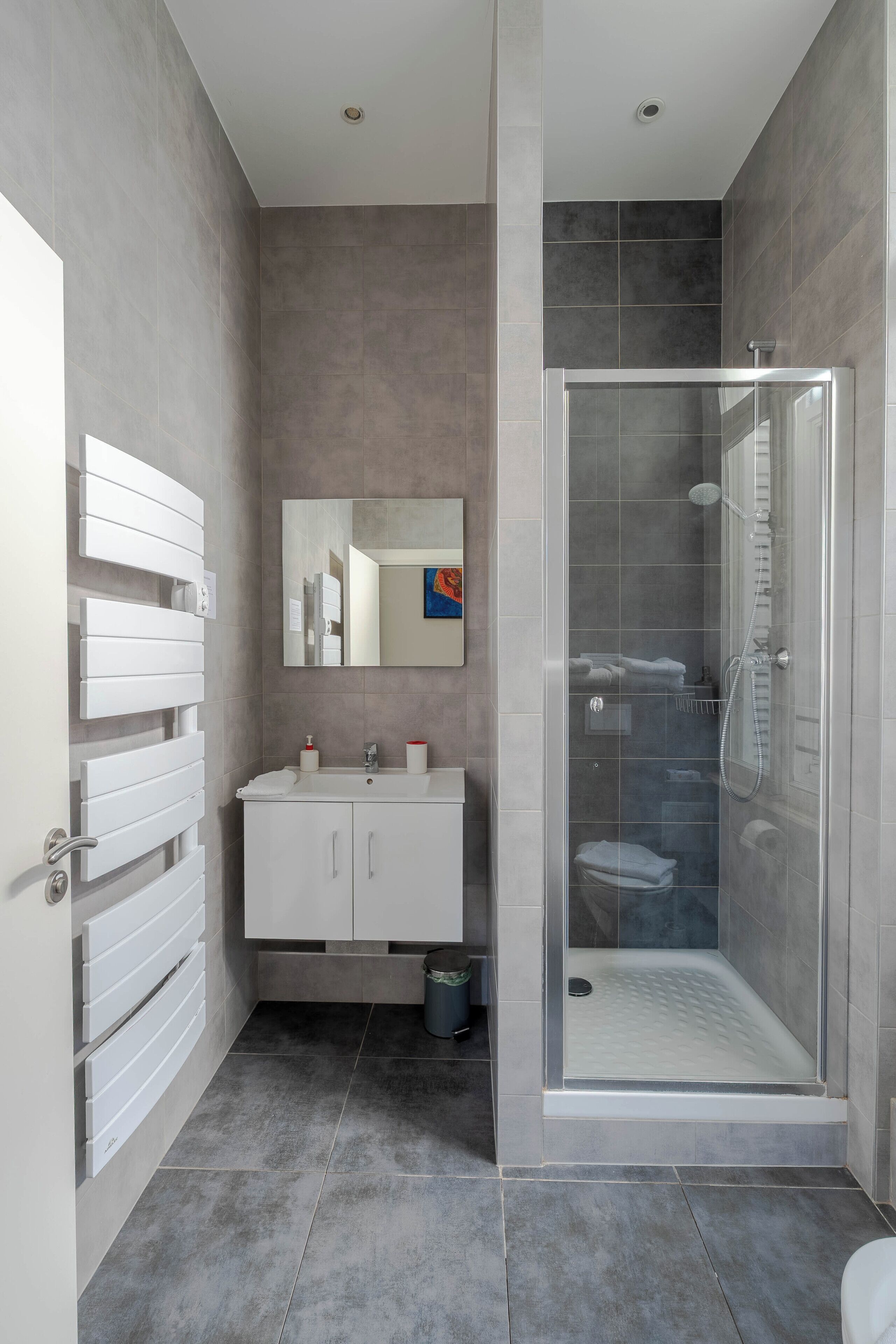 Un baño moderno con ducha de vidrio, tocador blanco con espejo y suelo de baldosas.