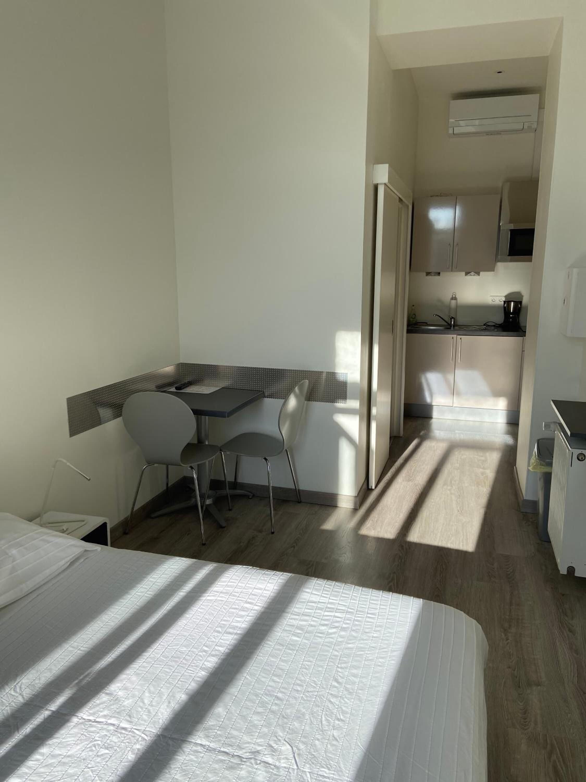 Una camera d'albergo piccola e funzionale, con un letto, una scrivania, una sedia e angolo cottura.