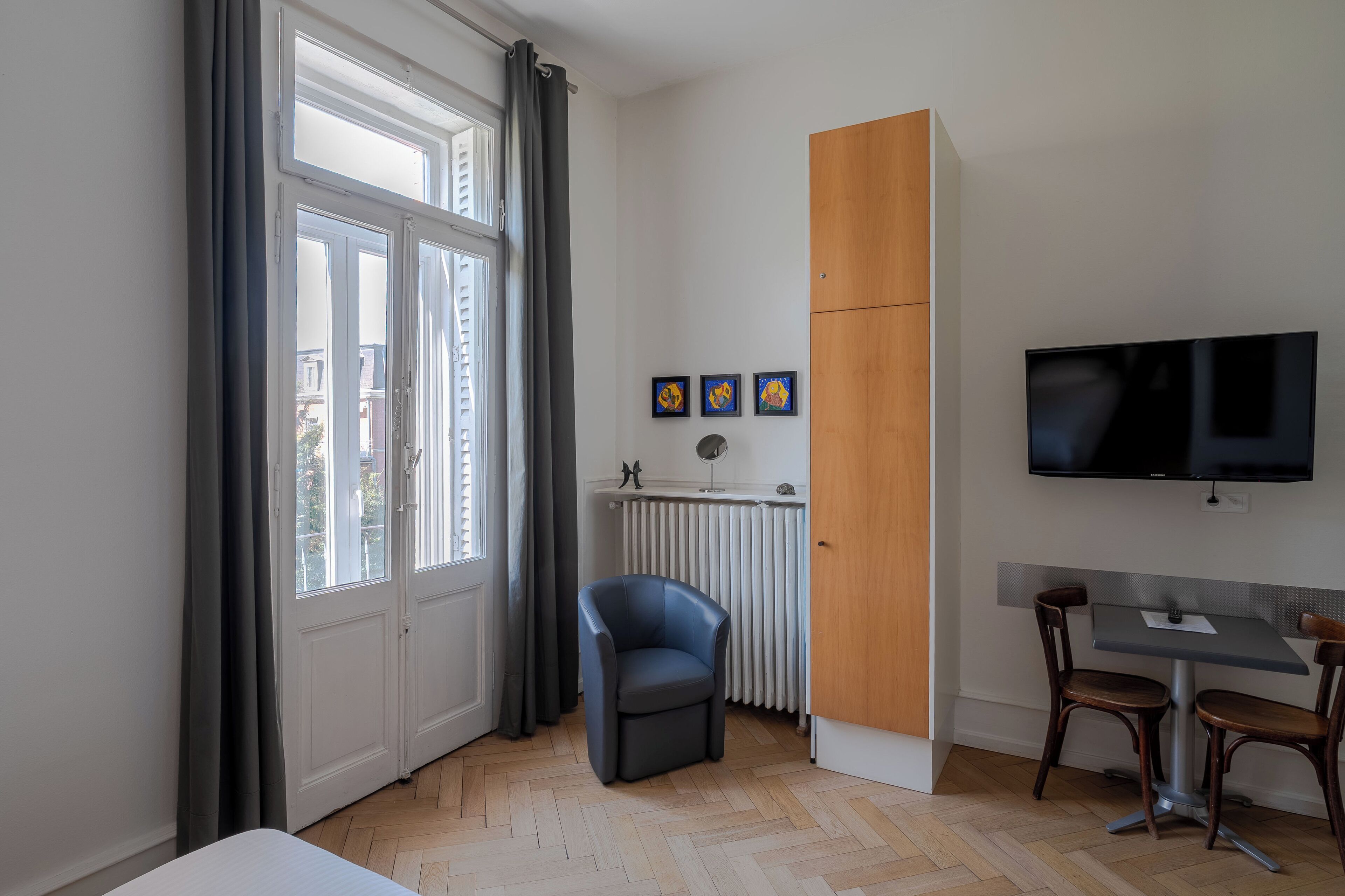 Ett modernt rum med ett stort fönster, en stol, ett bord med två stolar, en tv och ett element.
