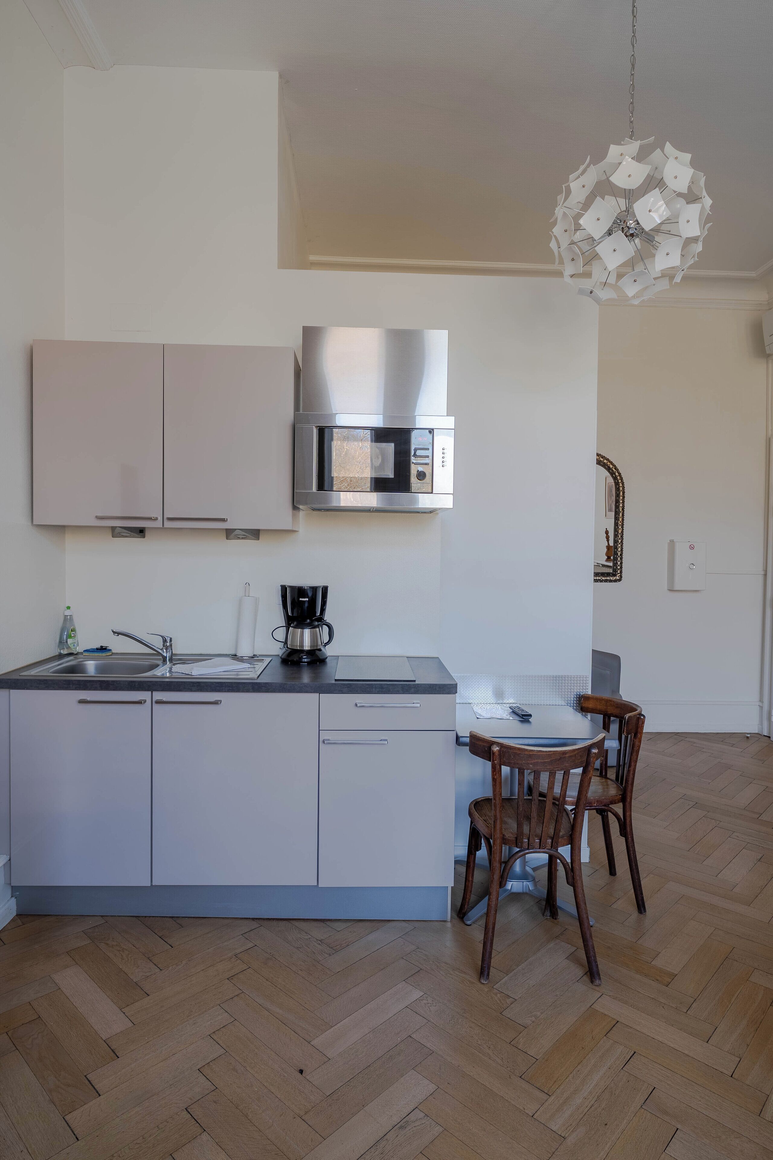 A modern kitchen with a stainless steel microwave, a coffee maker, and wooden chairs.