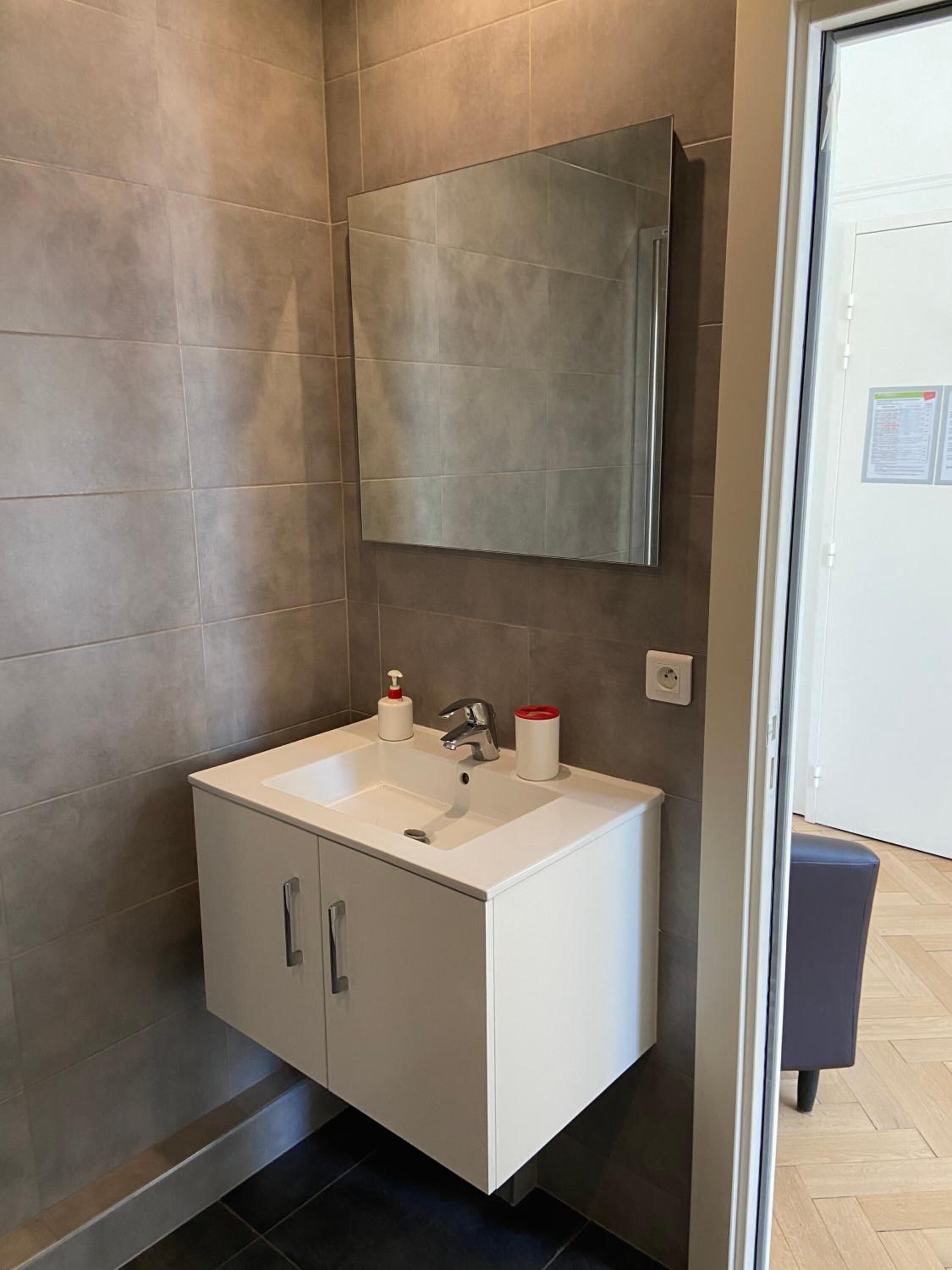 Un baño moderno con un lavamanos blanco, un espejo y un armario.
