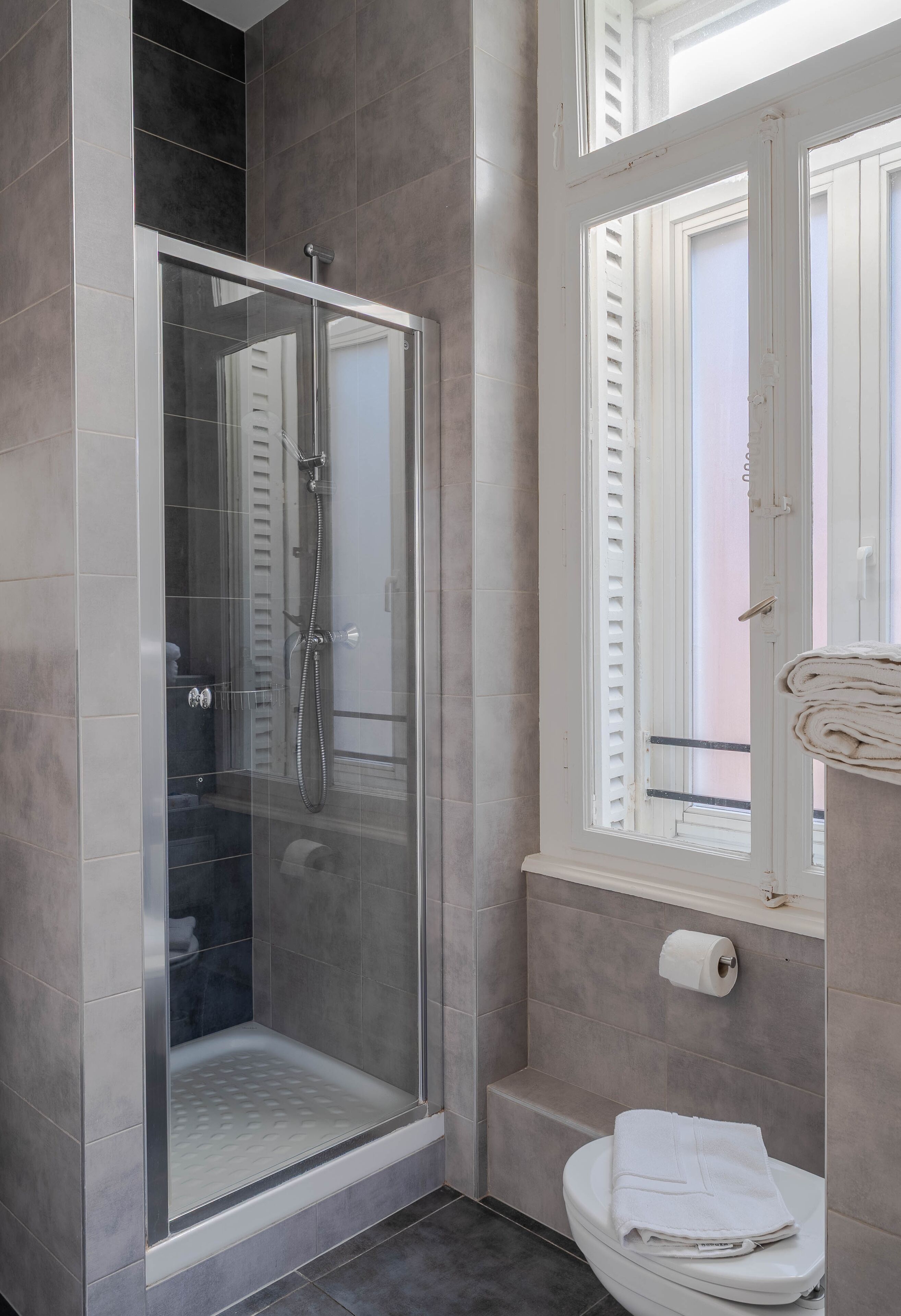 Une salle de bain moderne avec une douche à parois de verre, des toilettes et une fenêtre avec des volets.
