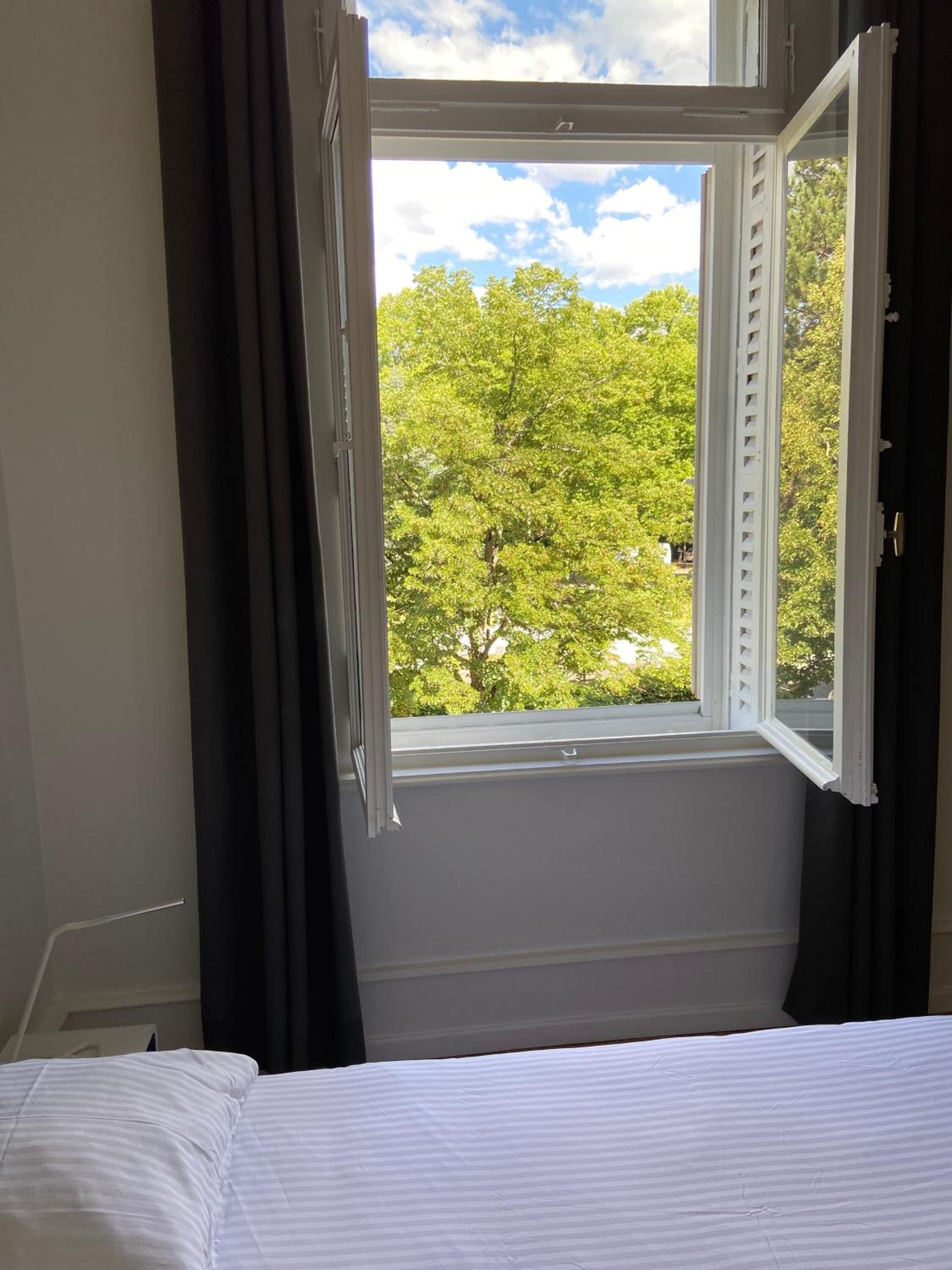 A room with a bed, a window with curtains, and a view of trees.