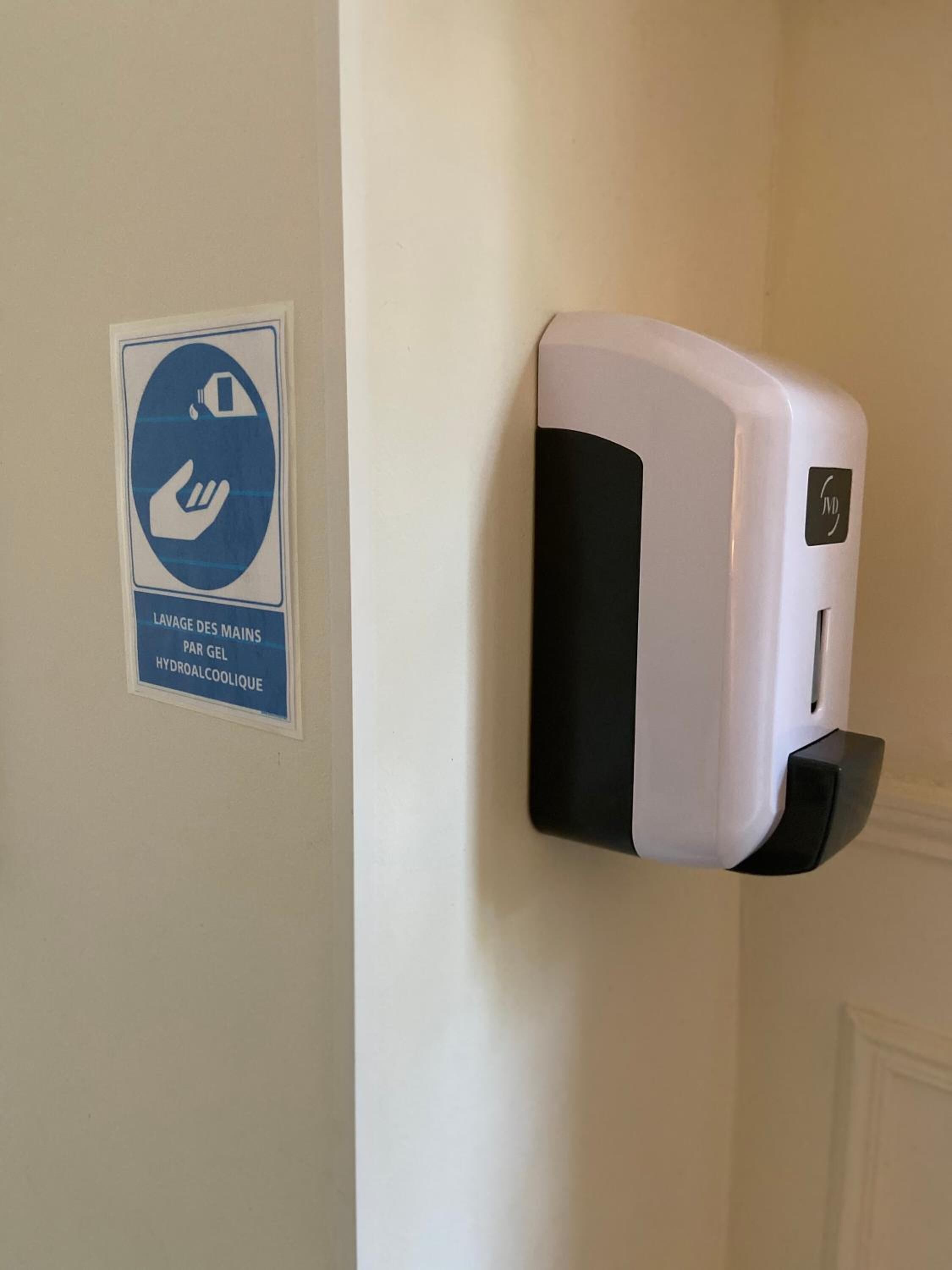 A hand sanitizer dispenser mounted on a wall next to a sign indicating hand washing with soap.