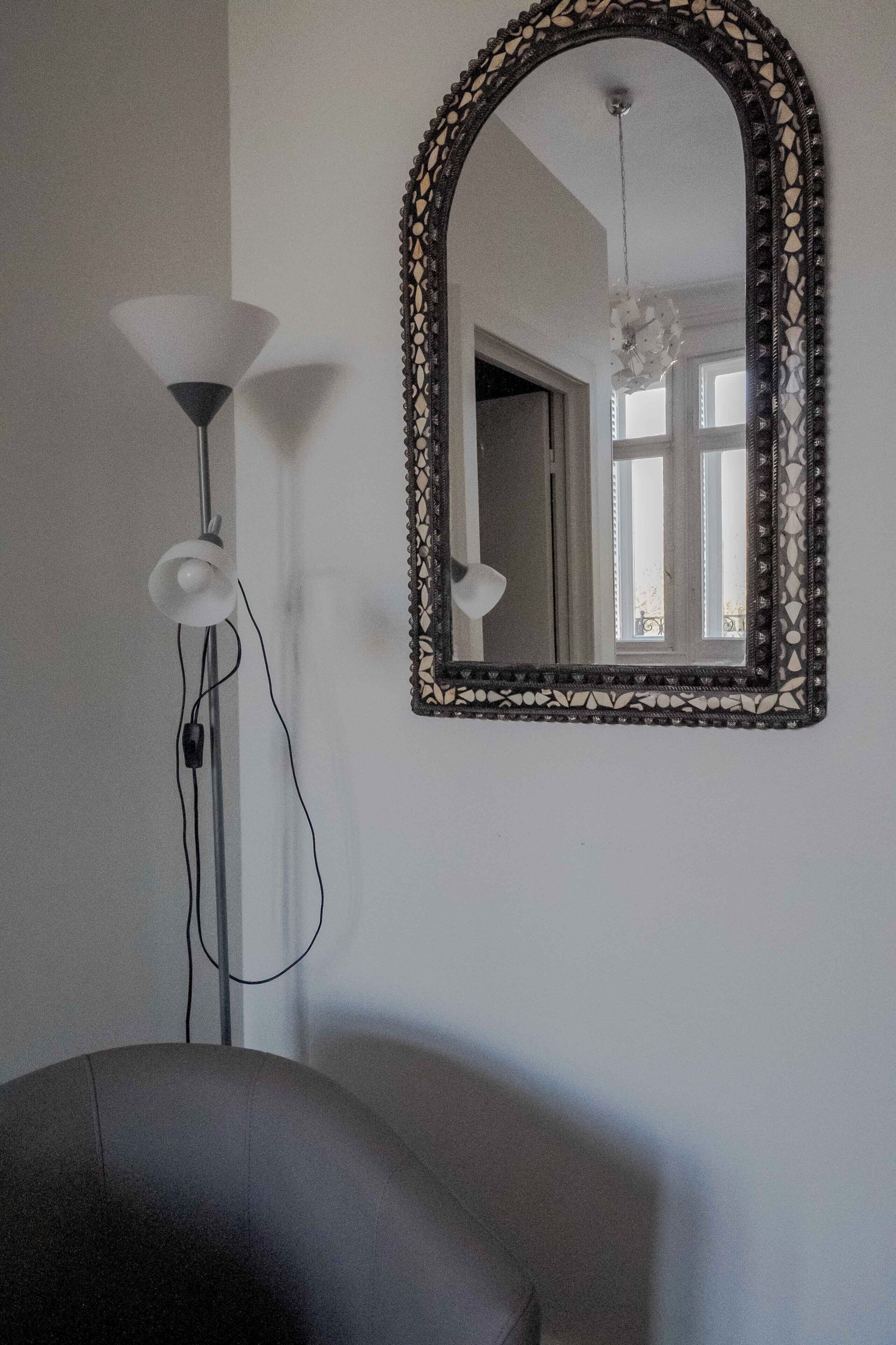 A room with a large mirror, a floor lamp, and a chair.