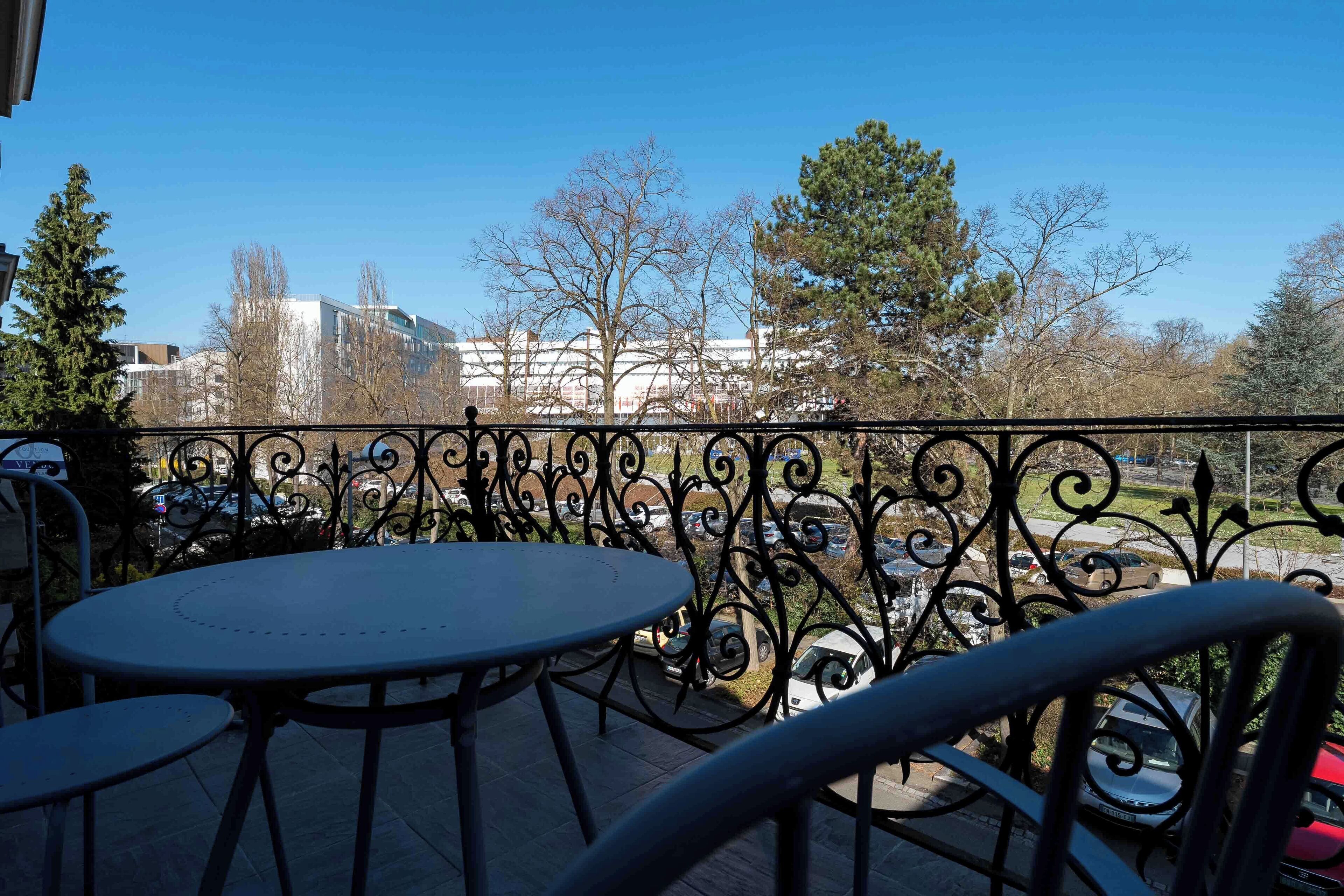 Un balcon avec une balustrade en métal, une table ronde et des chaises.