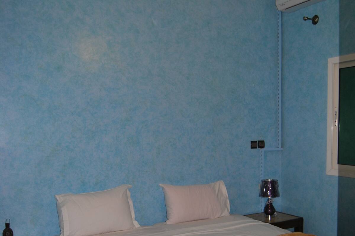 A hotel room with a bed, a nightstand, a lamp, and a wall-mounted air conditioner.