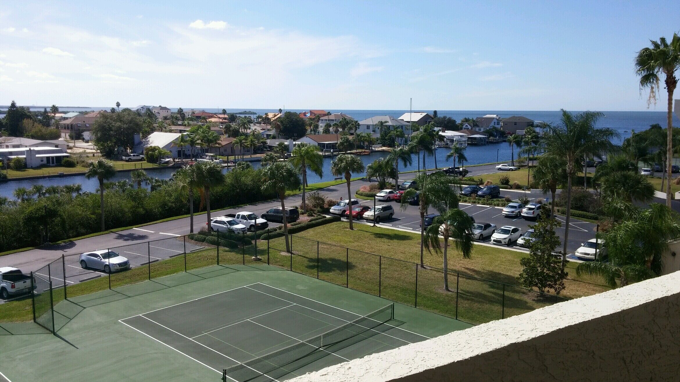 A tennis court with a view of a marina and ocean.