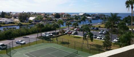 A tennis court with a view of a marina and ocean.