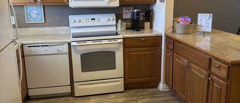 A kitchen with wooden cabinets, a microwave, an oven, a coffee maker, and a welcome sign.