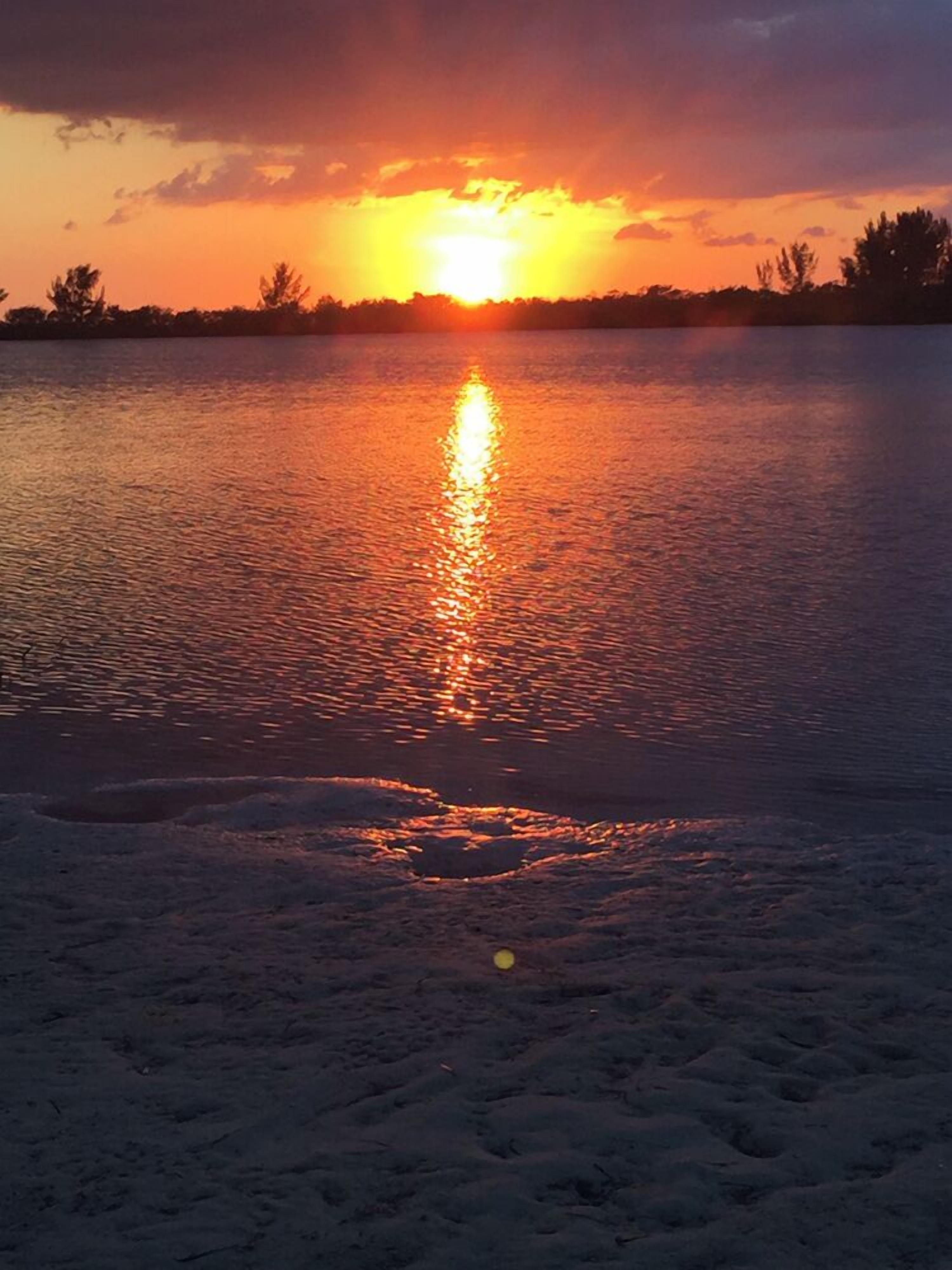A sunset over a calm body of water with a sandy foreground.