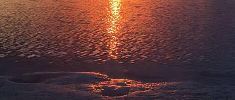 A sunset over a calm body of water with a sandy foreground.