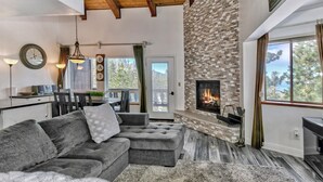 A cozy living room with a stone fireplace, a large gray sectional sofa, and a dining area with a wooden table and chairs. - Mv17 amazing lake view  spacious ski cabin (Stateline)