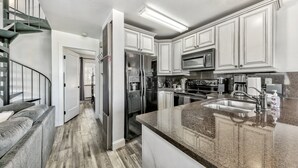 A modern kitchen with white cabinets, stainless steel appliances, a granite countertop, and a staircase leading to another level. - Mv17 amazing lake view  spacious ski cabin (Stateline)
