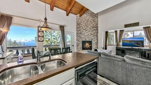 A modern kitchen with a granite countertop, stainless steel sink, and a dishwasher. There is a stone wall with a fireplace and a TV mounted above it. - Mv17 amazing lake view  spacious ski cabin (Stateline)