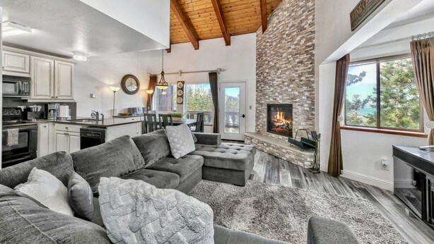 A modern living room with a stone fireplace, grey sofas, and a kitchen in the background. - Mv17 amazing lake view  spacious ski cabin (Stateline)