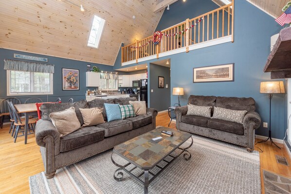 A spacious living area with two grey sofas, a coffee table, and a kitchen in the background. - Swiss-Style Dog Friendly Chalet w/ Hot Tub (SWANTON)