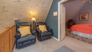 A room with a sloped ceiling, two leather recliners with cushions, a bed with an orange bedspread, a patterned rug, and a lamp. - Swiss-Style Dog Friendly Chalet w/ Hot Tub (SWANTON)
