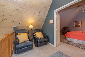 A room with a sloped ceiling, two leather recliners with cushions, a bed with an orange bedspread, a patterned rug, and a lamp. - Swiss-Style Dog Friendly Chalet w/ Hot Tub (SWANTON)