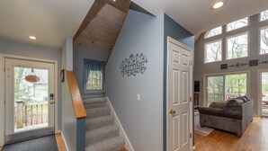 A staircase leading to a second floor, a welcome sign on the wall, a wooden door, and a gray sofa in a room with wooden flooring. - Swiss-Style Dog Friendly Chalet w/ Hot Tub (SWANTON)