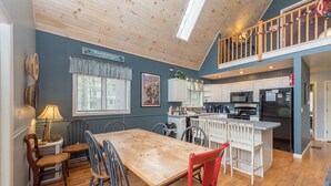 A spacious kitchen with a wooden table and chairs, a dining area, and a lofted space with a railing. - Swiss-Style Dog Friendly Chalet w/ Hot Tub (SWANTON)