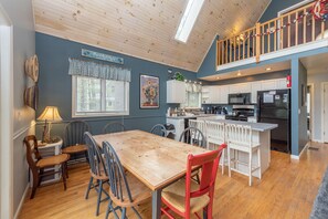 A spacious kitchen with a wooden table and chairs, a dining area, and a lofted space with a railing. - Swiss-Style Dog Friendly Chalet w/ Hot Tub (SWANTON)