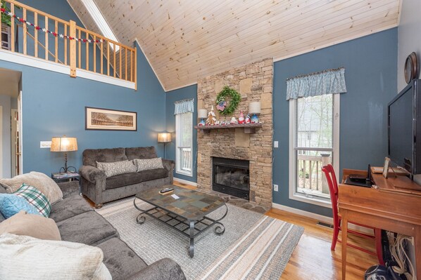 A cozy living room with a stone fireplace, a wooden staircase, and a blue wall. - Swiss-Style Dog Friendly Chalet w/ Hot Tub (SWANTON)