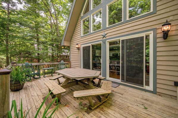 A wooden deck with picnic tables and a large window overlooking a forested area. - Swiss-Style Dog Friendly Chalet w/ Hot Tub (SWANTON)