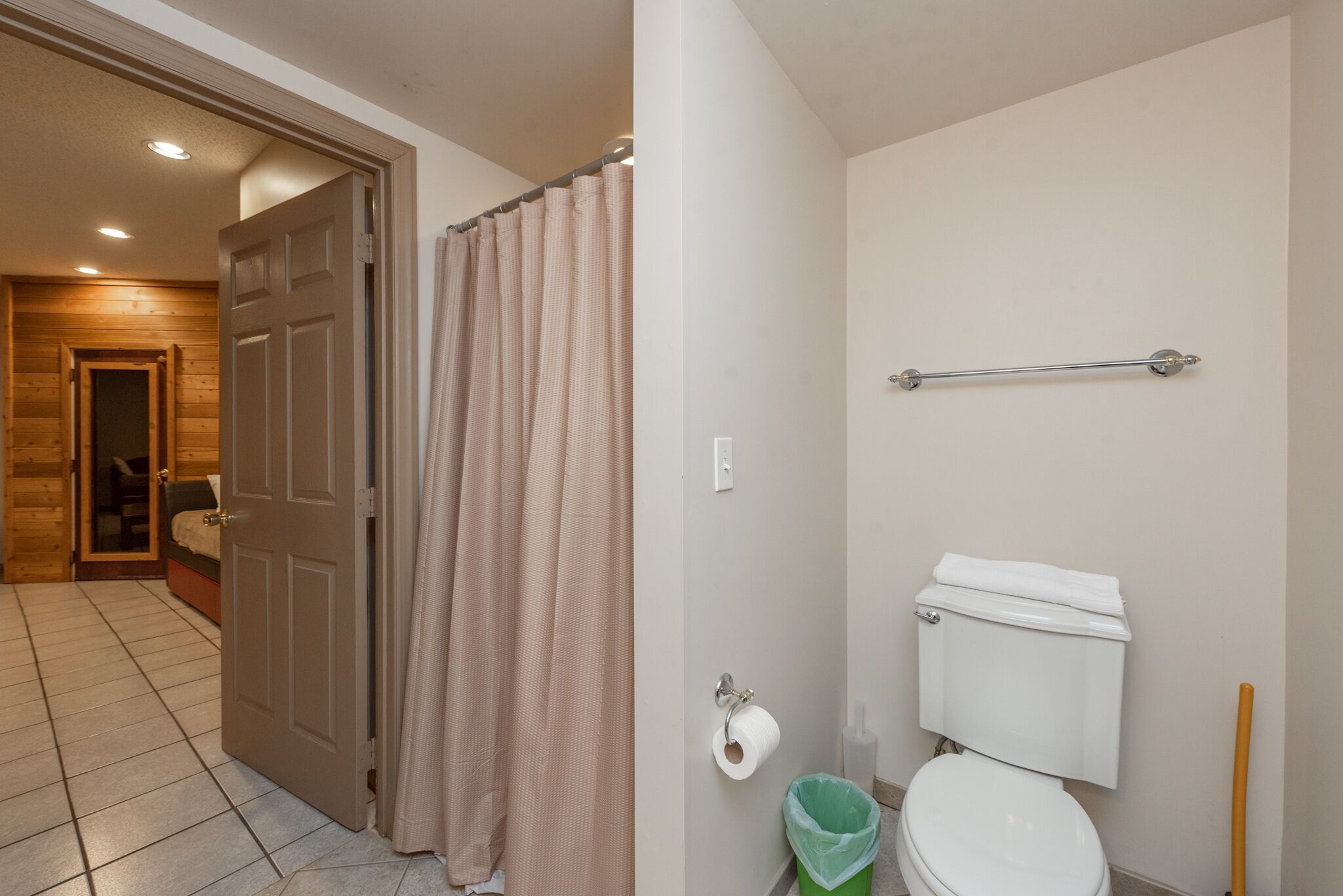 A bathroom with a toilet, a green trash bin, a shower curtain, and a towel rack.