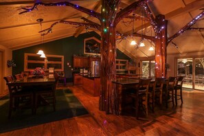 Zona pranzo con un centro tavola a forma di albero in legno, arredi in legno e luci a stringa.