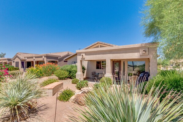 A residential area with houses featuring stucco exteriors, a patio with outdoor furniture, and a variety of desert plants.