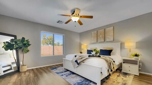 A bedroom with a bed, bedside tables, a ceiling fan, a window with blinds, and a large plant. - 3BR w pool, golf community, dog friendly (Maricopa)