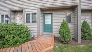 A two-story building with a green door, a stone accent wall, and a small porch.