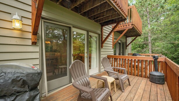 A wooden deck with Adirondack chairs, a grill, and a wooden staircase leading to a deck.