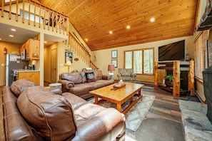 A spacious living room with a wooden ceiling, leather sofas, a wooden coffee table, and a stone fireplace.