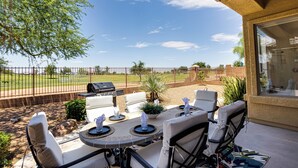 Une terrasse extérieure avec une table et des chaises, un barbecue et une vue sur une cour clôturée.