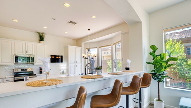 Une cuisine moderne avec des meubles blancs, un grand îlot central doté de tabourets, et une vue sur l’extérieur grâce à de grandes fenêtres.