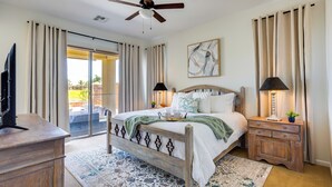 Une chambre à coucher comprenant un lit, un ventilateur de plafond, une table de chevet avec une lampe, un téléviseur et une vue sur l’extérieur.