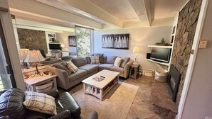 A modern living room with a sectional sofa, a coffee table, a TV, and a fireplace. - Super Location Between Lionshead and Vail Village - Outdoor Pool and Hot Tub (Vail)