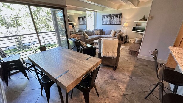 A modern living room with a large window, a dining area with a wooden table and chairs, and a cozy seating area with a sofa and armchairs. - Super Location Between Lionshead and Vail Village - Outdoor Pool and Hot Tub (Vail)
