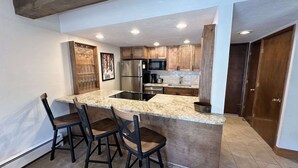 A modern kitchen with a central island, wooden cabinets, stainless steel appliances, and a tiled backsplash. - Centrally Located Vail Condo with Fireplace and Views of the Outdoor Pool (Vail)