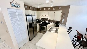 A compact kitchen with a refrigerator, stove, microwave, and a sink. - Relax and enjoy your tropical getaway in this lovely Silver-rated condo! (Saint Augustine)