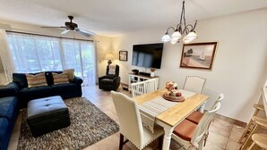 A living room with a sofa, ottoman, and a dining area with a table and chairs. - Enjoy family time in this Gold-rated condo with quick access to the beach! (Saint Augustine)