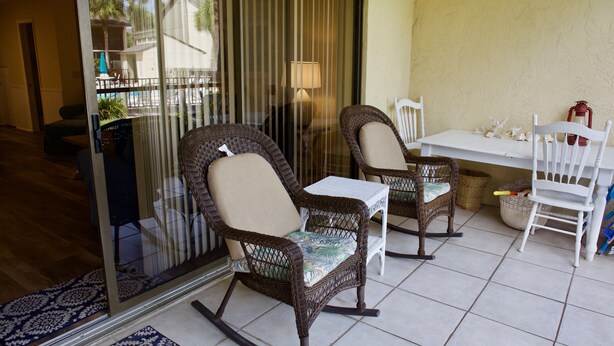 Un patio con sillas mecedoras de mimbre, una mesa blanca y una lámpara.