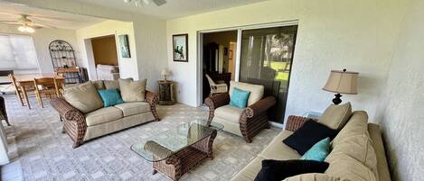 A living room with two sofas, a glass coffee table, and a ceiling fan.